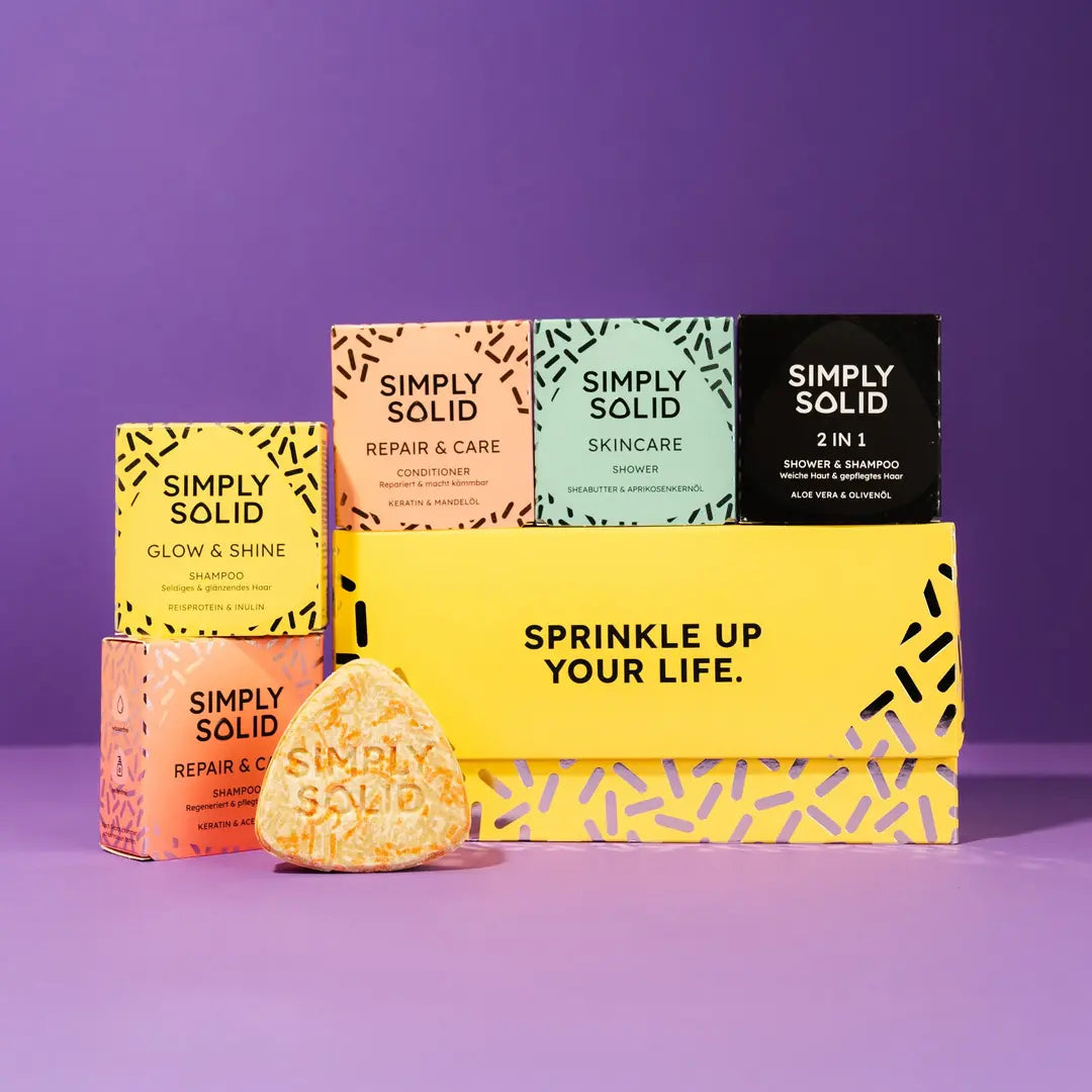 Simply Solid Geschenkset vor einem Hintergrund in violett, mit einem Repair and Care Solid im Vordergrund. Die geschenkbox ist mit dem Slogan Sprinkle up your life. bedruckt und ist in sonnengelb ein echter Hingucker auf dem Geschenketisch.